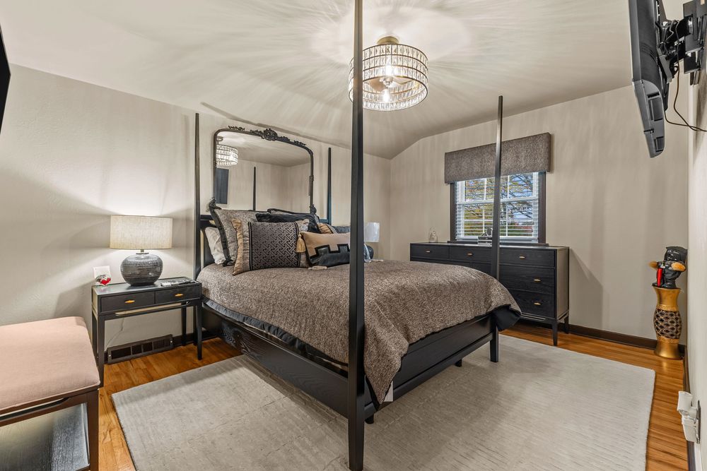 Elegant master bedroom with four-poster bed, vaulted ceiling, chandelier, and hardwood floors.