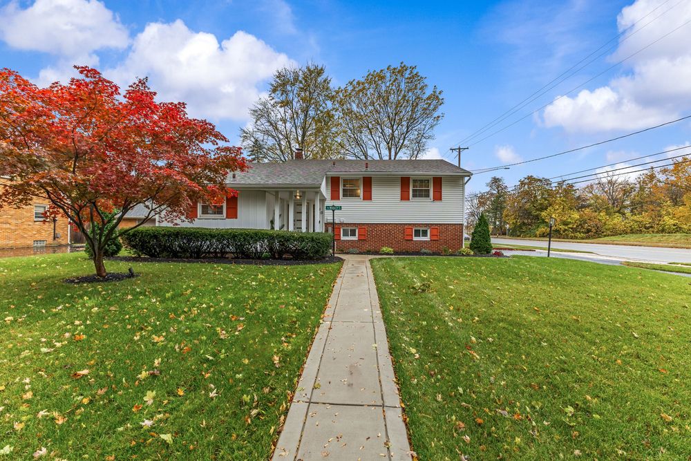 Brick split-level home with red shutters, manicured lawn, and vibrant red maple tree in front yard.