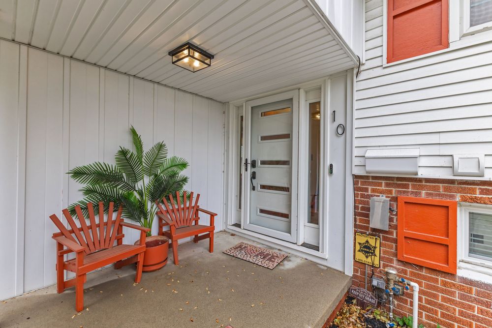 Welcoming covered front porch with red Adirondack chairs, modern white door, and brick exterior accent.