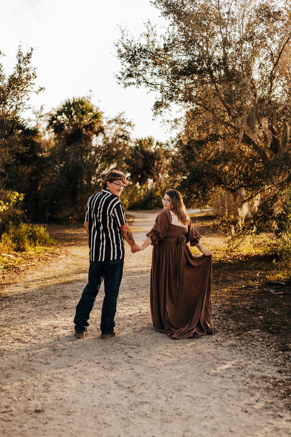 A couple walking along a sandy path at sunset, holding hands in a romantic autumn setting.