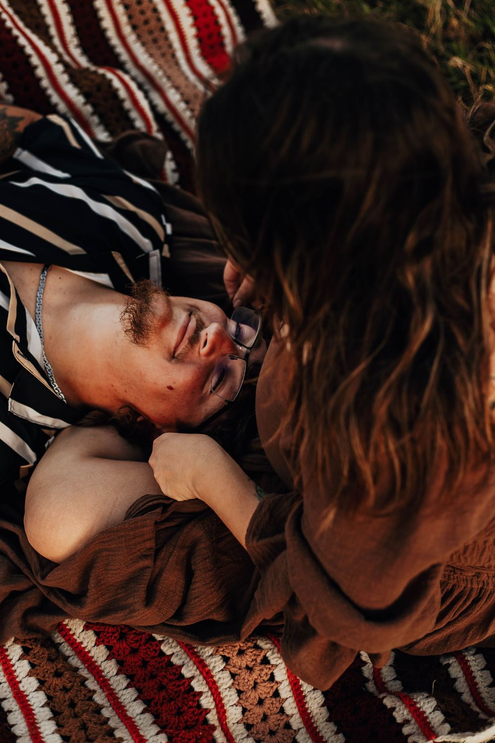 Intimate moment captured on a striped blanket showing two people sharing a tender, joyful interaction.