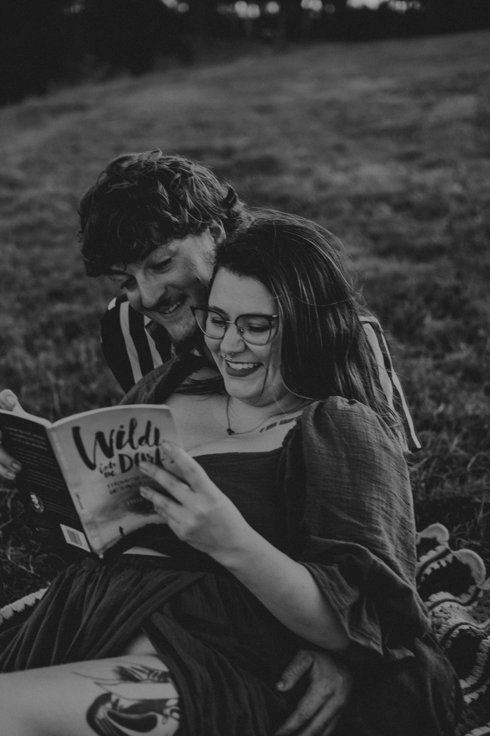 Two people lying in grass reading a book together in black and white photography.