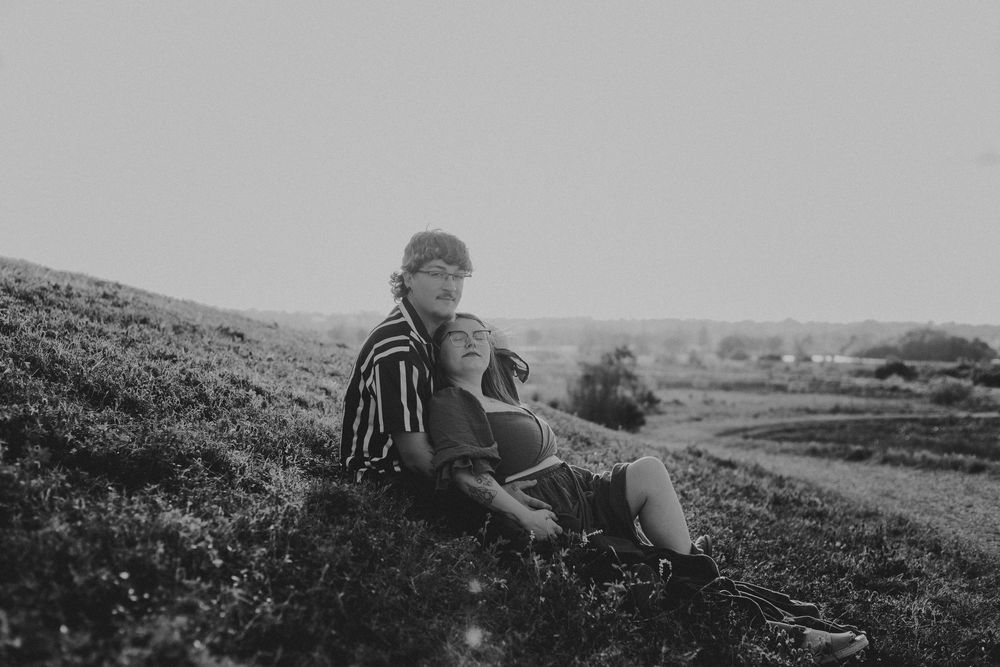 A person in a striped shirt sits on a grassy hillside in black and white.