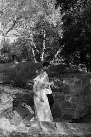 Black and white photo of couple by stone wall in garden setting.