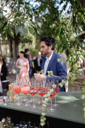 Row of pink cocktails lined up on bar with fresh garnishes at outdoor event.
