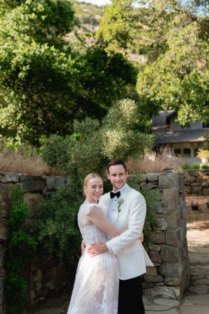 A couple poses for a romantic portrait against a rustic stone wall in a garden setting.