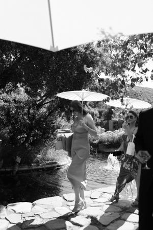 Black and white photo of guests with parasols on stone patio.