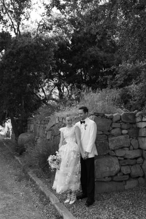 An elegant couple poses against a rustic stone wall during an outdoor wedding ceremony.
