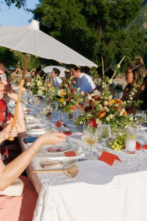 Outdoor wedding reception table with colorful floral arrangements and white tablecloths.