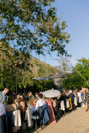 Elegant outdoor dining event with guests seated at long table against hillside backdrop.