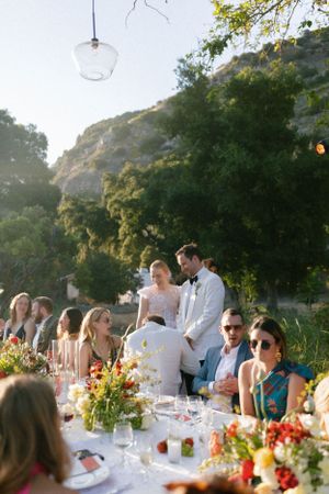 Guests enjoy an elegant outdoor wedding reception dinner with hanging glass lights and mountain views.