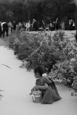 A black and white image showing a small figure near garden flowers at an outdoor event.