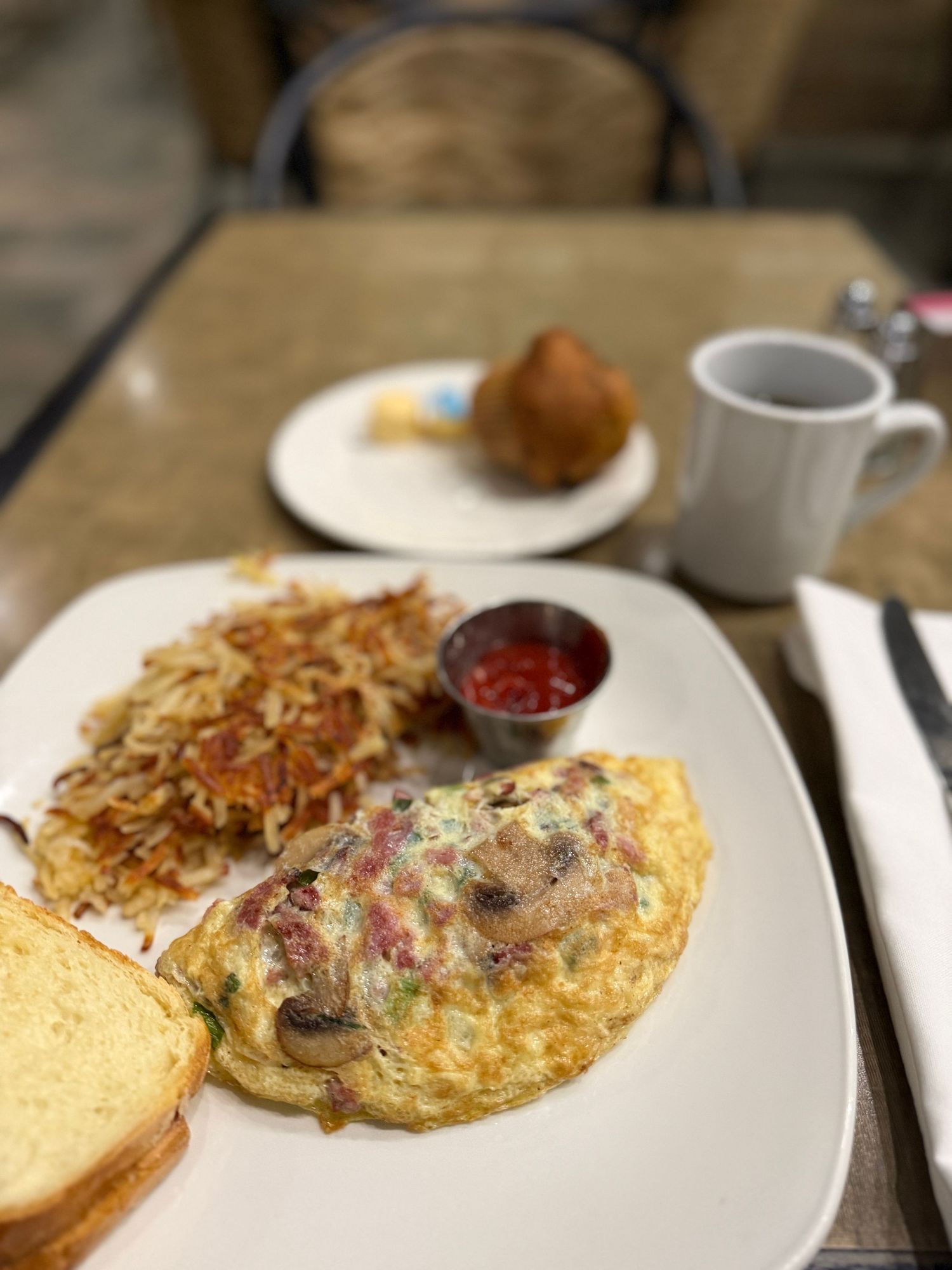A close-up view of a golden-brown omelet filled with mushrooms and cheese served on a white plate with sauce on the side.