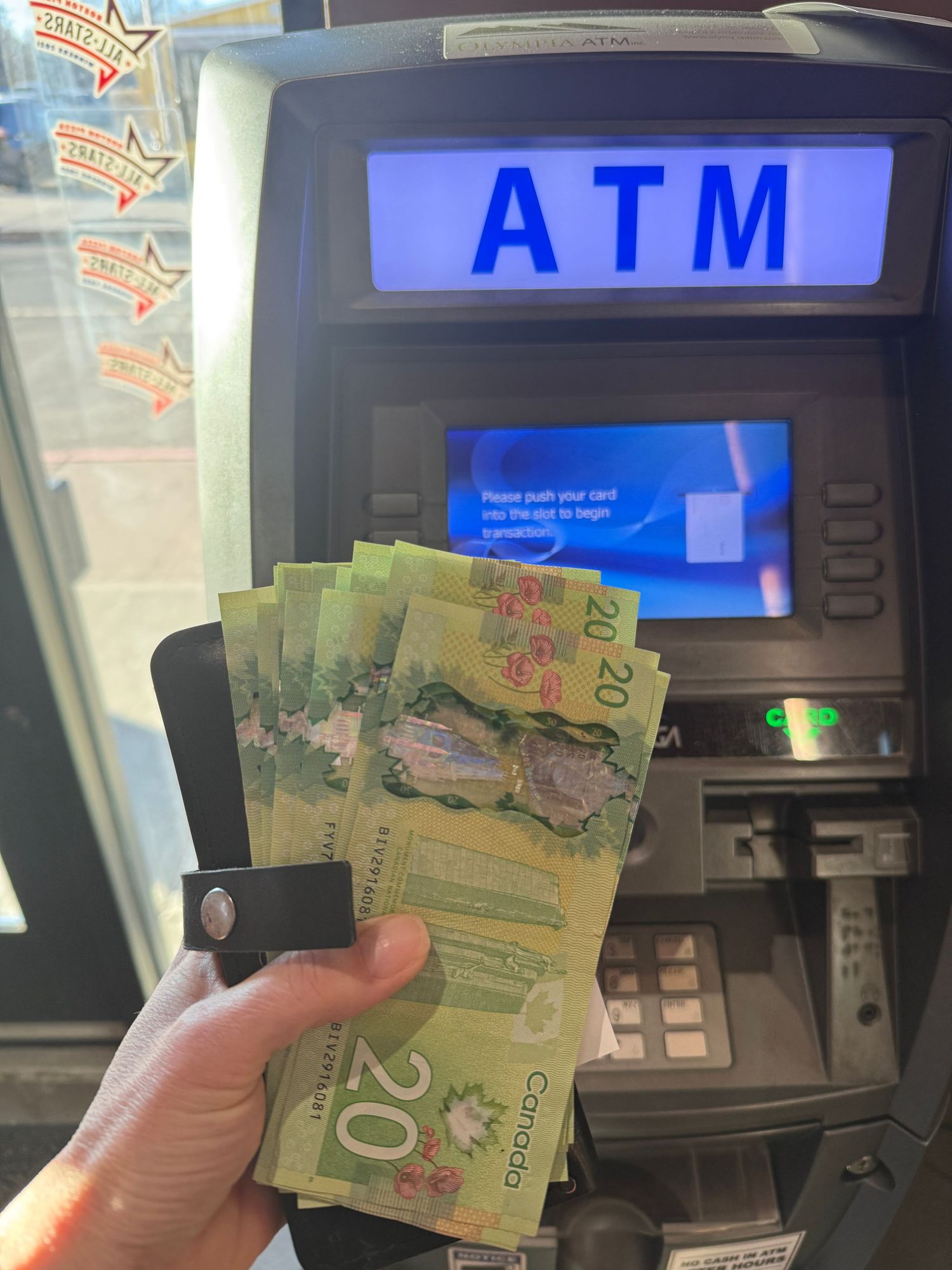 Canadian twenty dollar bills being withdrawn from an ATM machine at a bank.