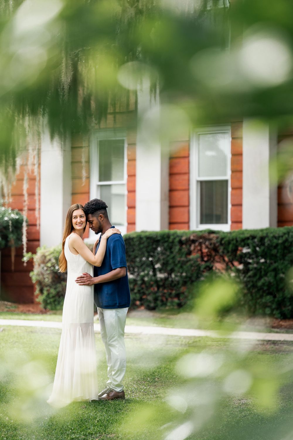 A couple shares intimate moments through soft focus foliage in an outdoor setting.