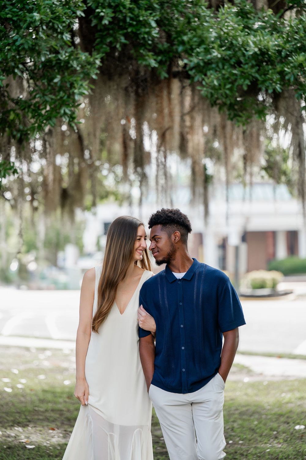 A couple poses for engagement photos under Spanish moss draped trees.