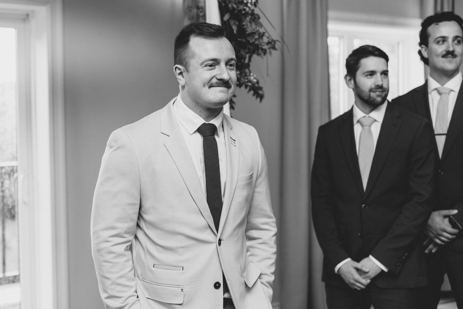 A vintage black and white photograph shows a group of men in formal attire standing together at a social gathering.
