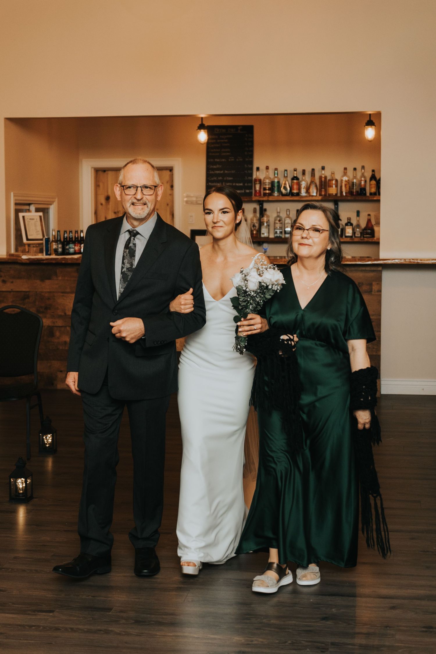 A group poses together in formal attire at a wedding reception with a bar backdrop in warm lighting.