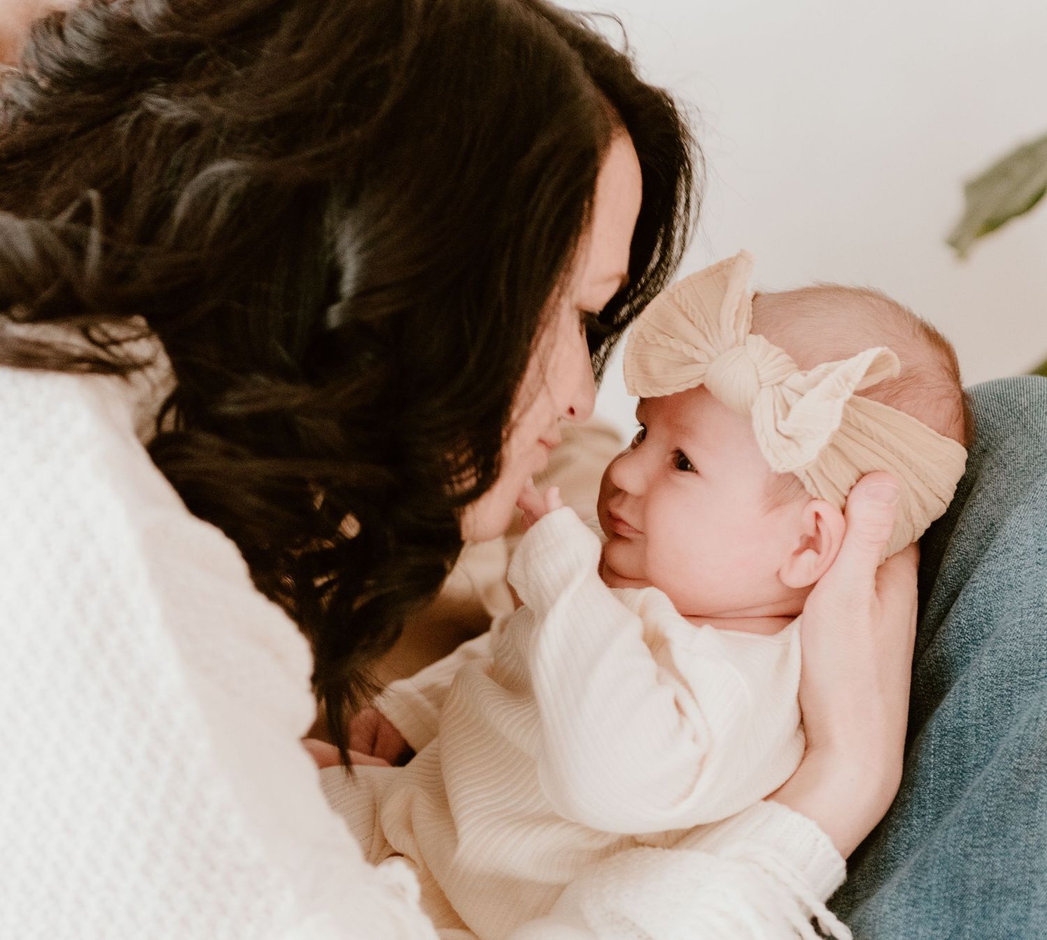Tender moment captured between parent and infant wearing a bow headband in soft natural lighting.