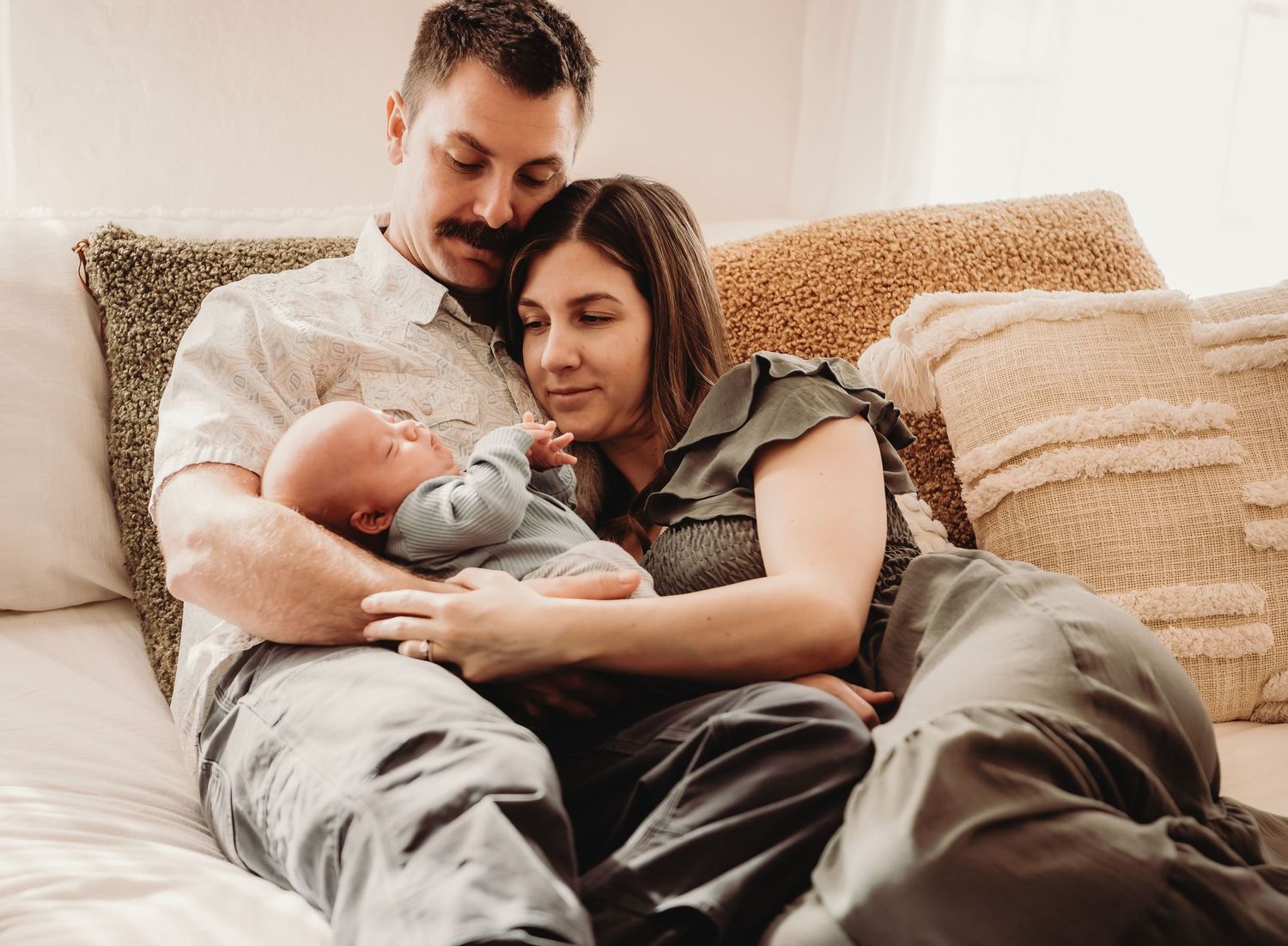Family shares tender moment while cuddling with newborn baby on couch.