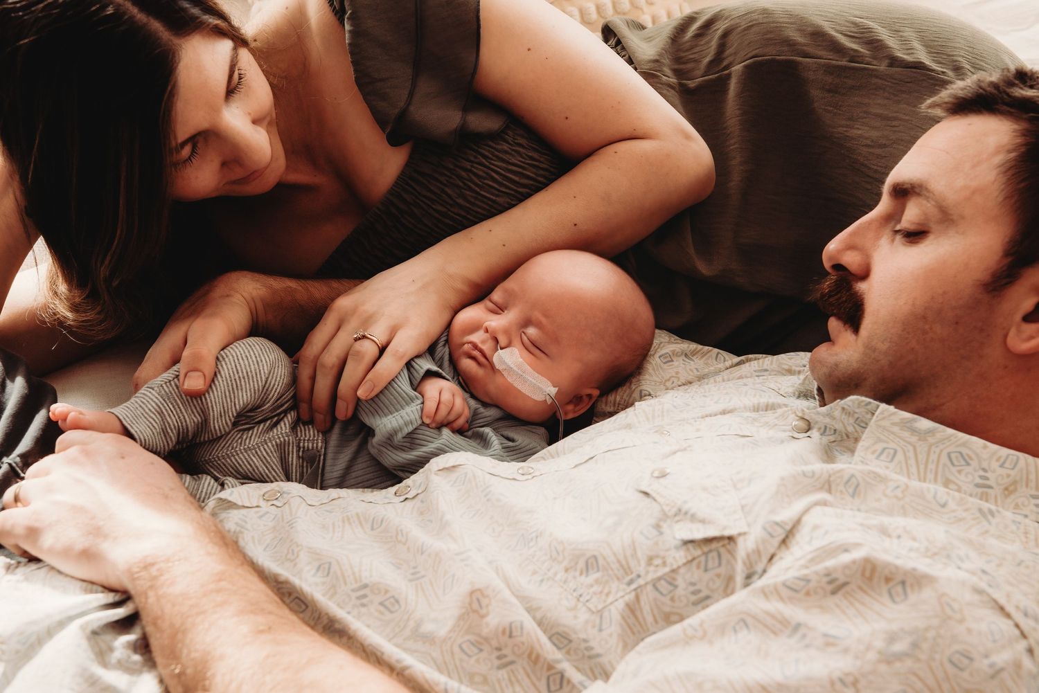 Intimate family moment captured as parents rest with newborn on bed.