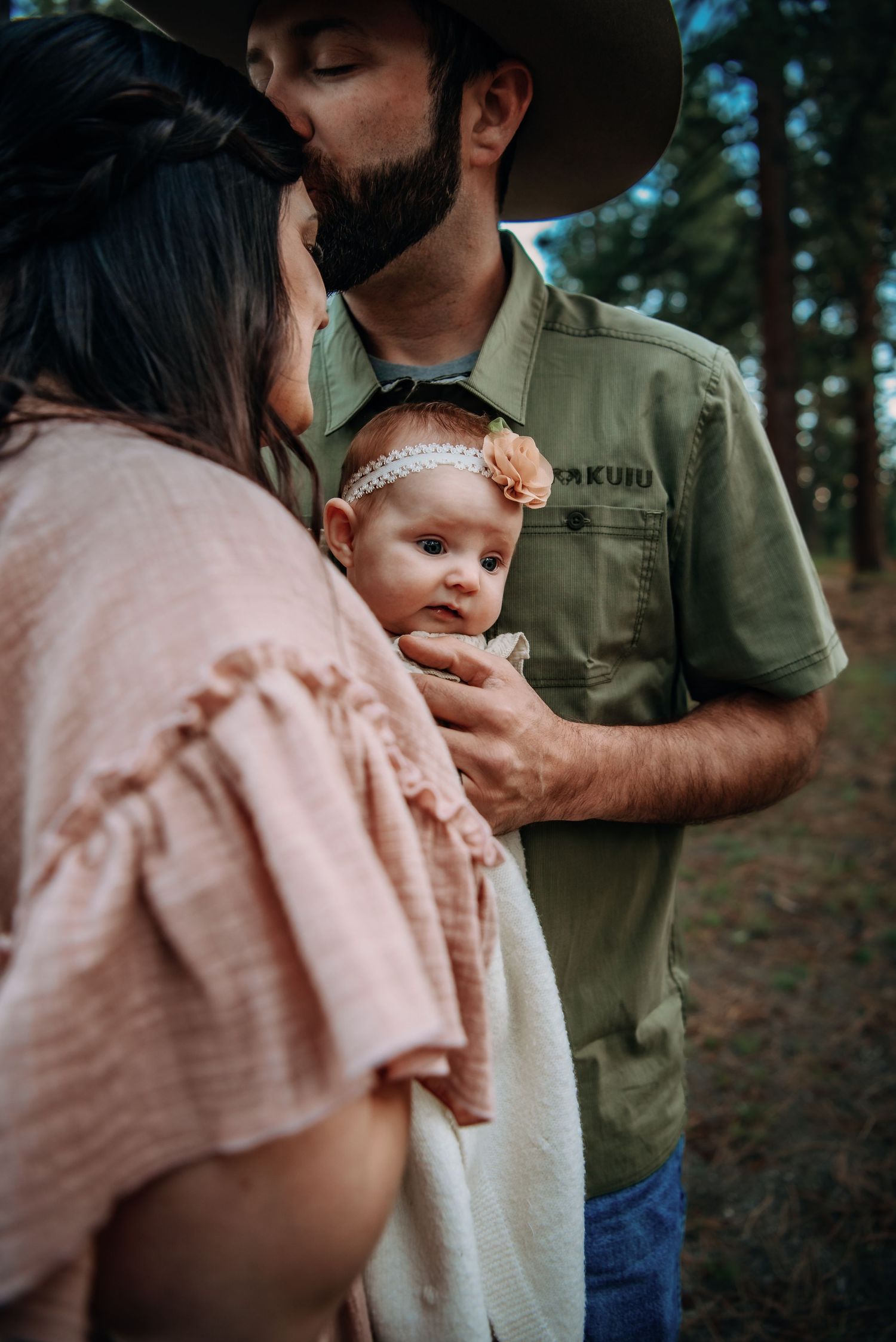 An intimate outdoor family portrait with a baby in a forest setting.