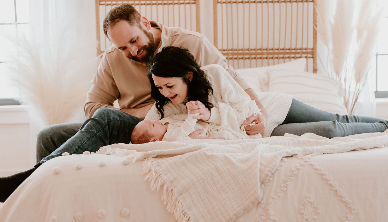 Family cuddles together on white bedding in casual intimate photo session.
