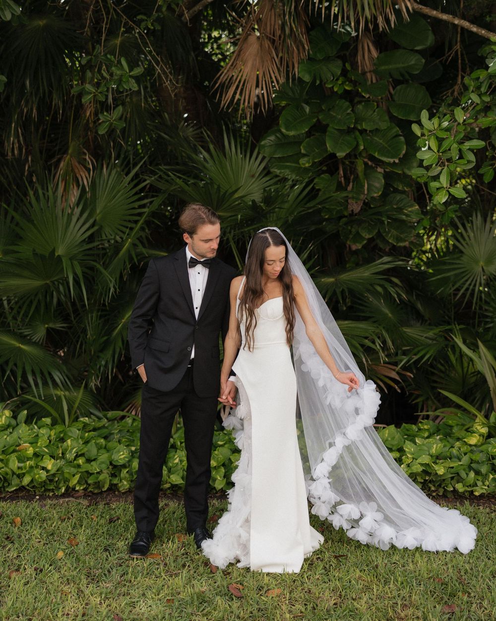 Wedding couple poses in front of lush tropical garden backdrop.