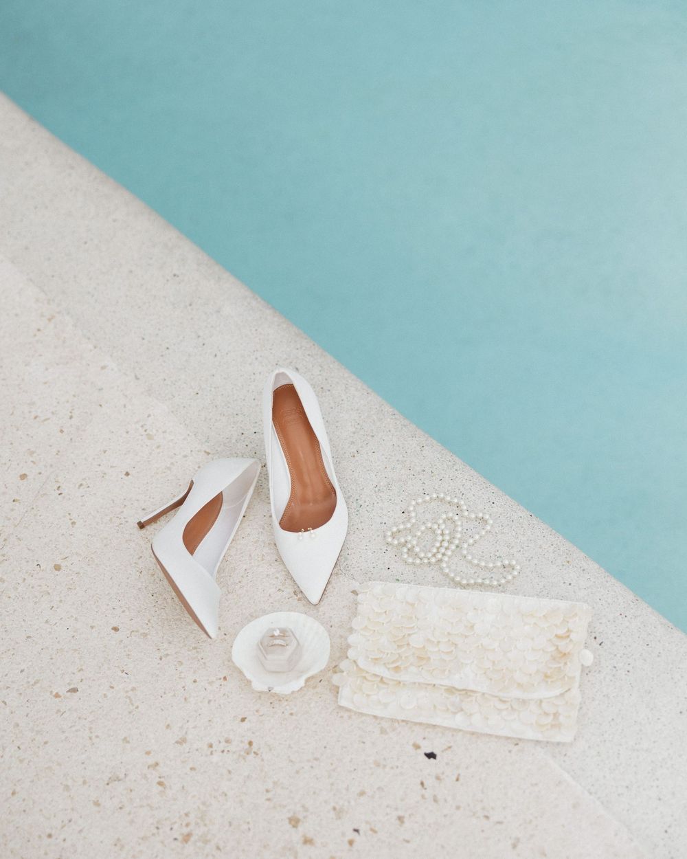White bridal shoes and clutch arranged on a light surface against turquoise background.