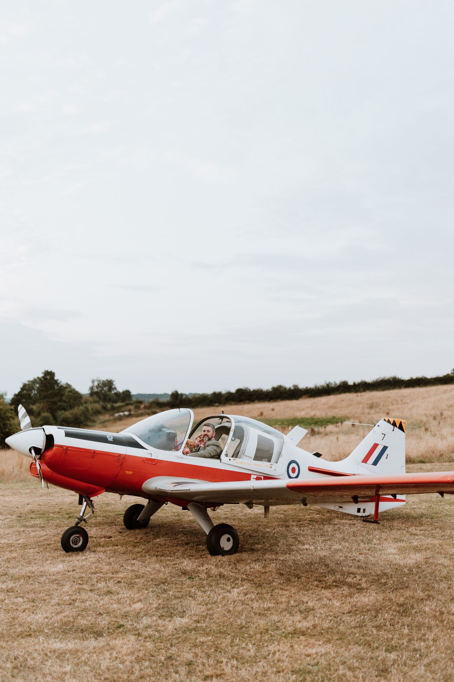 A vintage plane parked in a grassy field with newly married couple inside cockpit.