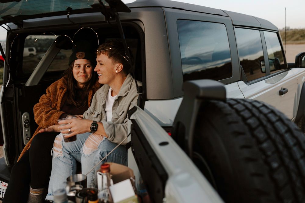 Two people sit together in a car while looking at something on a mobile device screen.