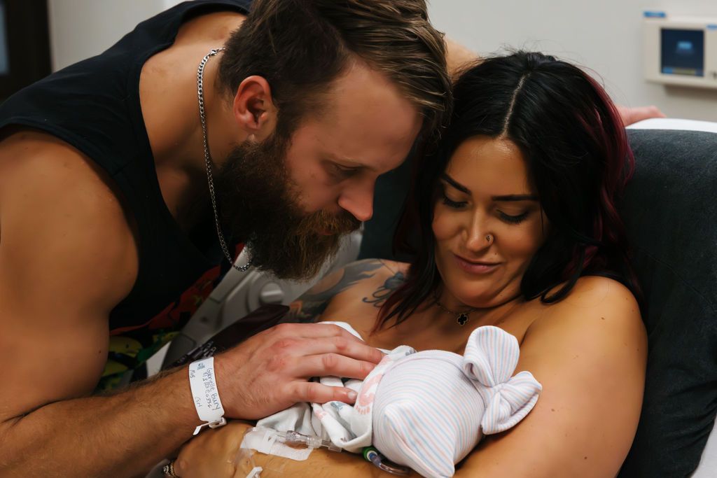 New parents tenderly holding their newborn baby in a hospital room, sharing a loving family moment.