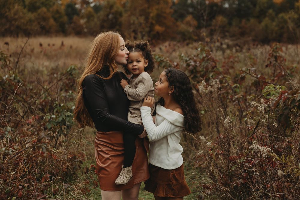 Two people share tender moments in an autumn field surrounded by dried foliage and warm earth tones.