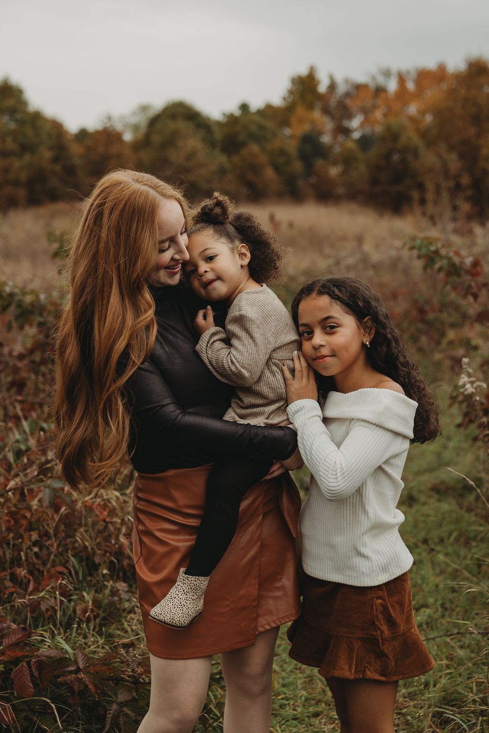 Three people share joyful moments together in a rustic autumn field setting.
