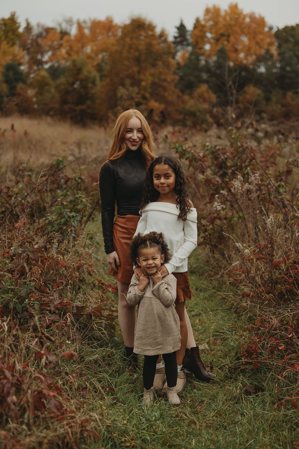 Three people stand together on a nature path surrounded by autumn foliage and brown ferns.