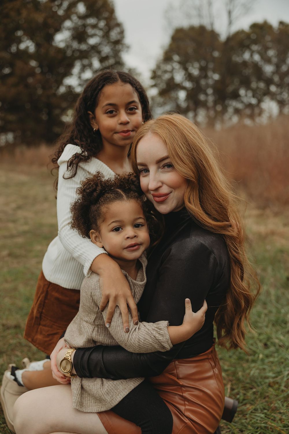 Mother and child share loving embraces while sitting in an autumn field wearing cozy sweaters.