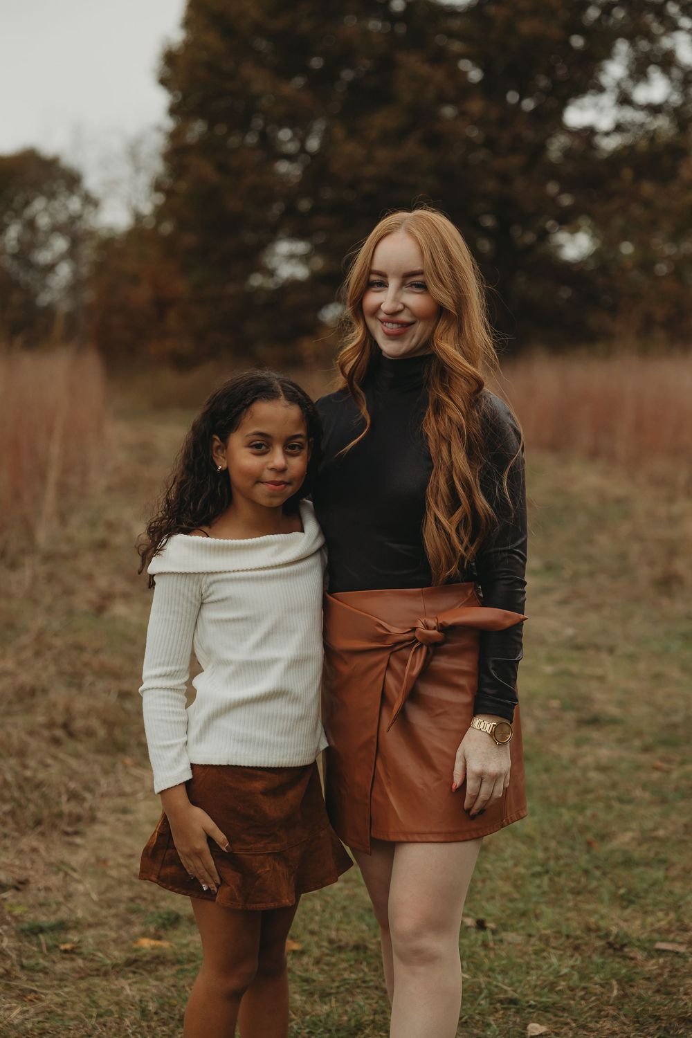 A heartwarming outdoor family photoshoot featuring coordinated autumn-colored outfits in a rustic field setting.