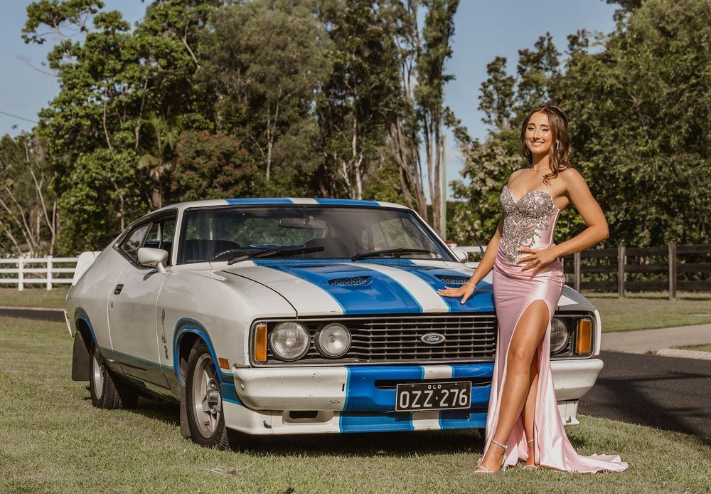 Formal/Graduation session young woman in elegant strapless pink and silver gown posing for photos beside a blue car outdoors in Caboolture.