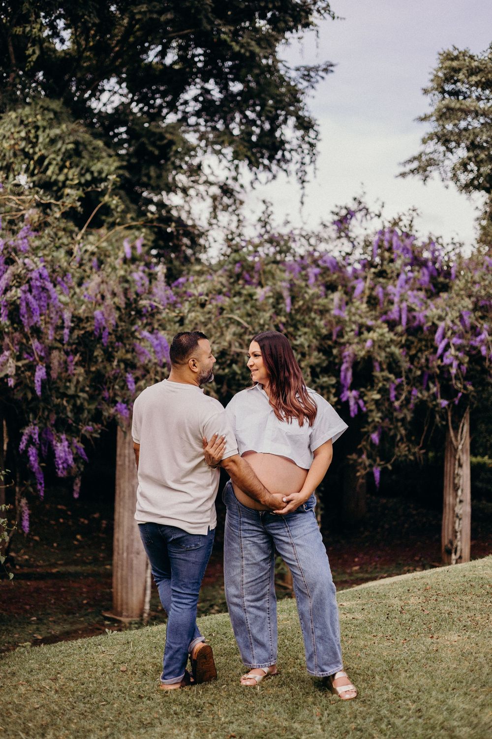 A couple poses together against a backdrop of blooming purple wisteria flowers in a garden setting.
