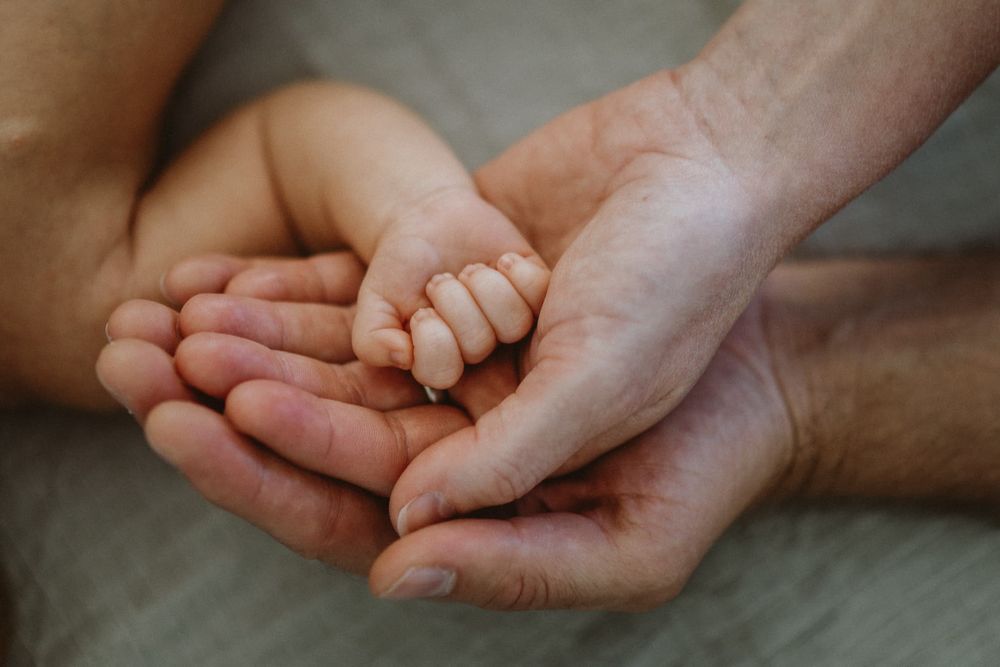 Mamma, pappa och nyfödd bebis händer. Bebisen ligger på en säng under en nyföddfotografering med Fotograf Veronica Eng i Mullsjö, Jönköping.