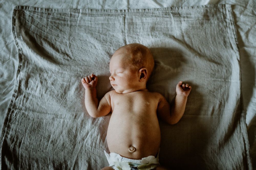 Nyfödd bebis ligger i fönsterljus på en säng, under en hemma fotografering i Jönköping med Fotograf Veronica Eng.