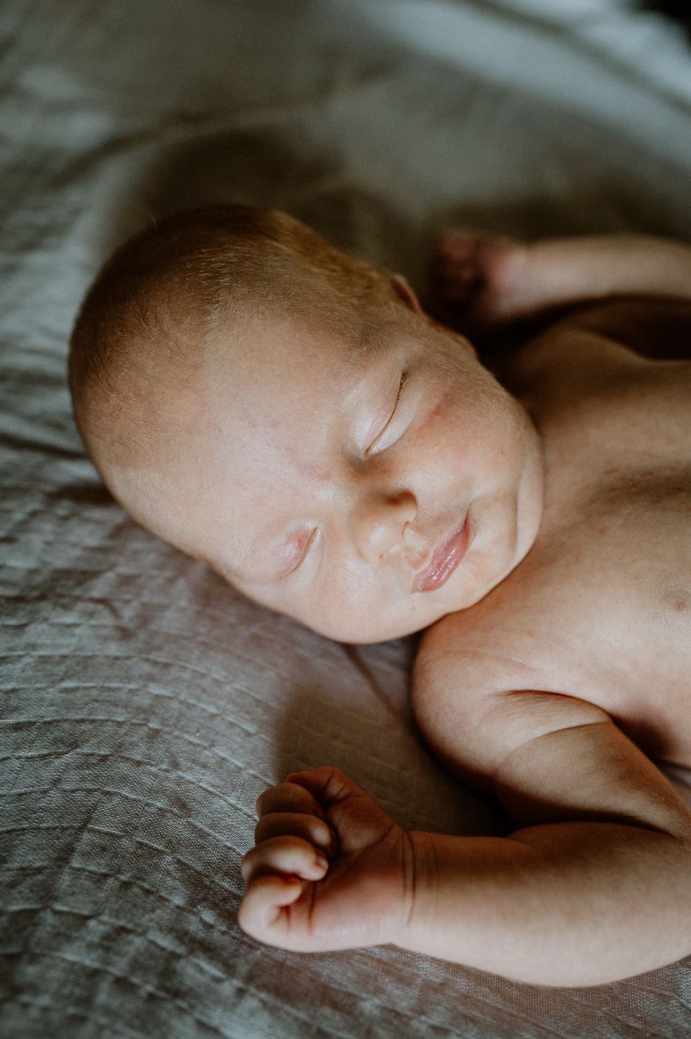 Nyfödd bebis ligger i fönsterljus på en säng, under en hemma fotografering i Jönköping med Fotograf Veronica Eng.