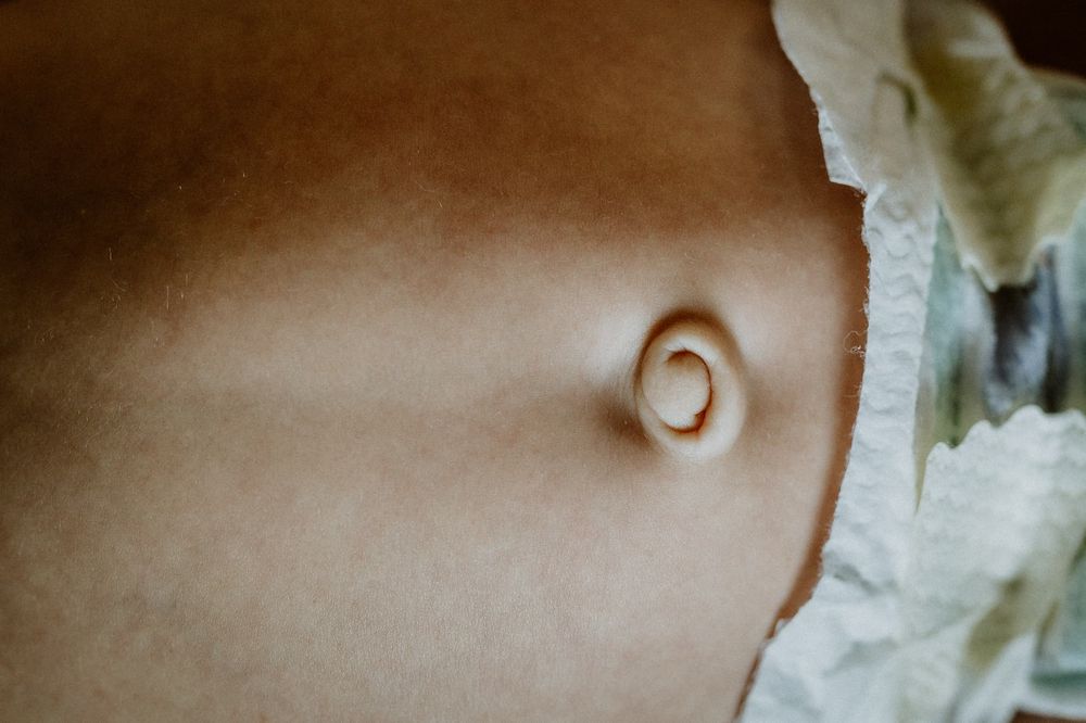 Detaljbild på nyfödd bebis navel. Bebisen har blöja. Den ligger på en säng under en nyföddfotografering i hemmet i Jönköping .