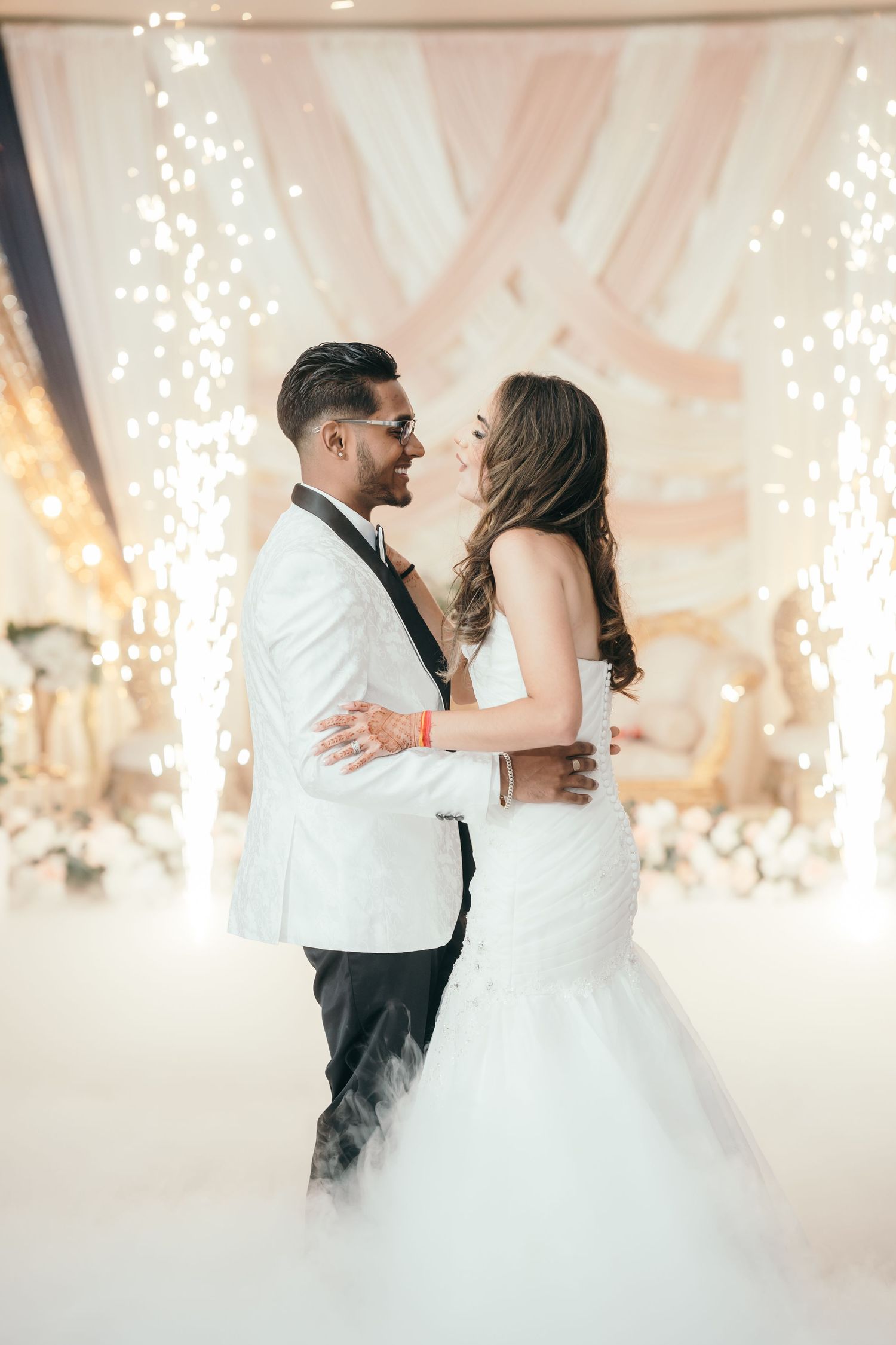 A romantic first dance between newlyweds surrounded by twinkling lights and soft white decor at their wedding reception.