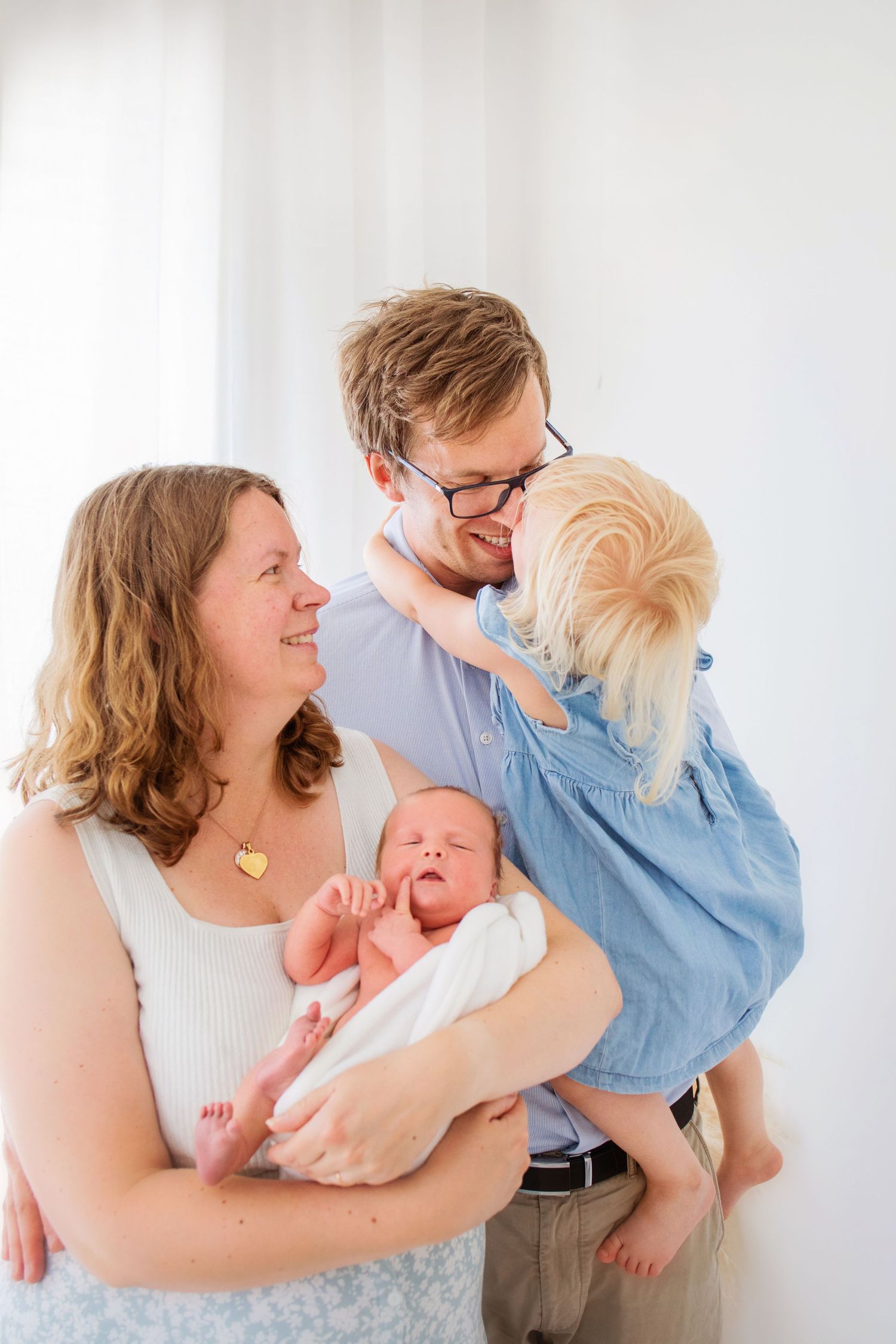 En familj i mjuka blåvita kläder delar ömma stunder i en ljus studiomiljö hos Fotograf Annelie Malmgren i Ängelholm
