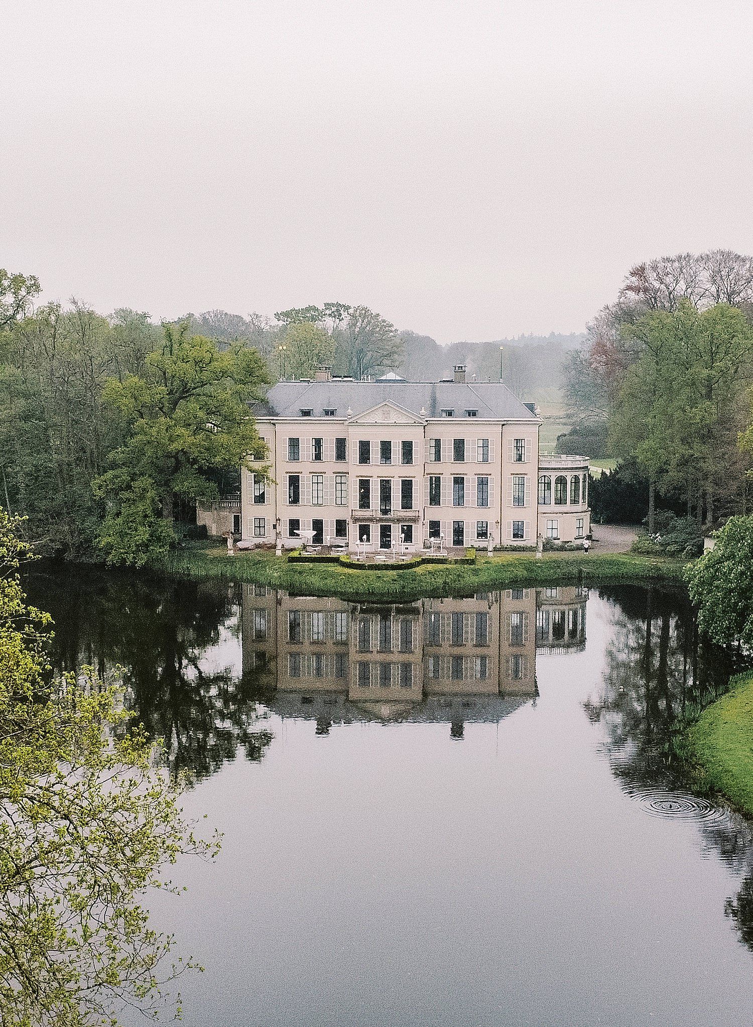 A series of panoramic views showing a stately building reflected in calm waters surrounded by lush trees on a misty day.