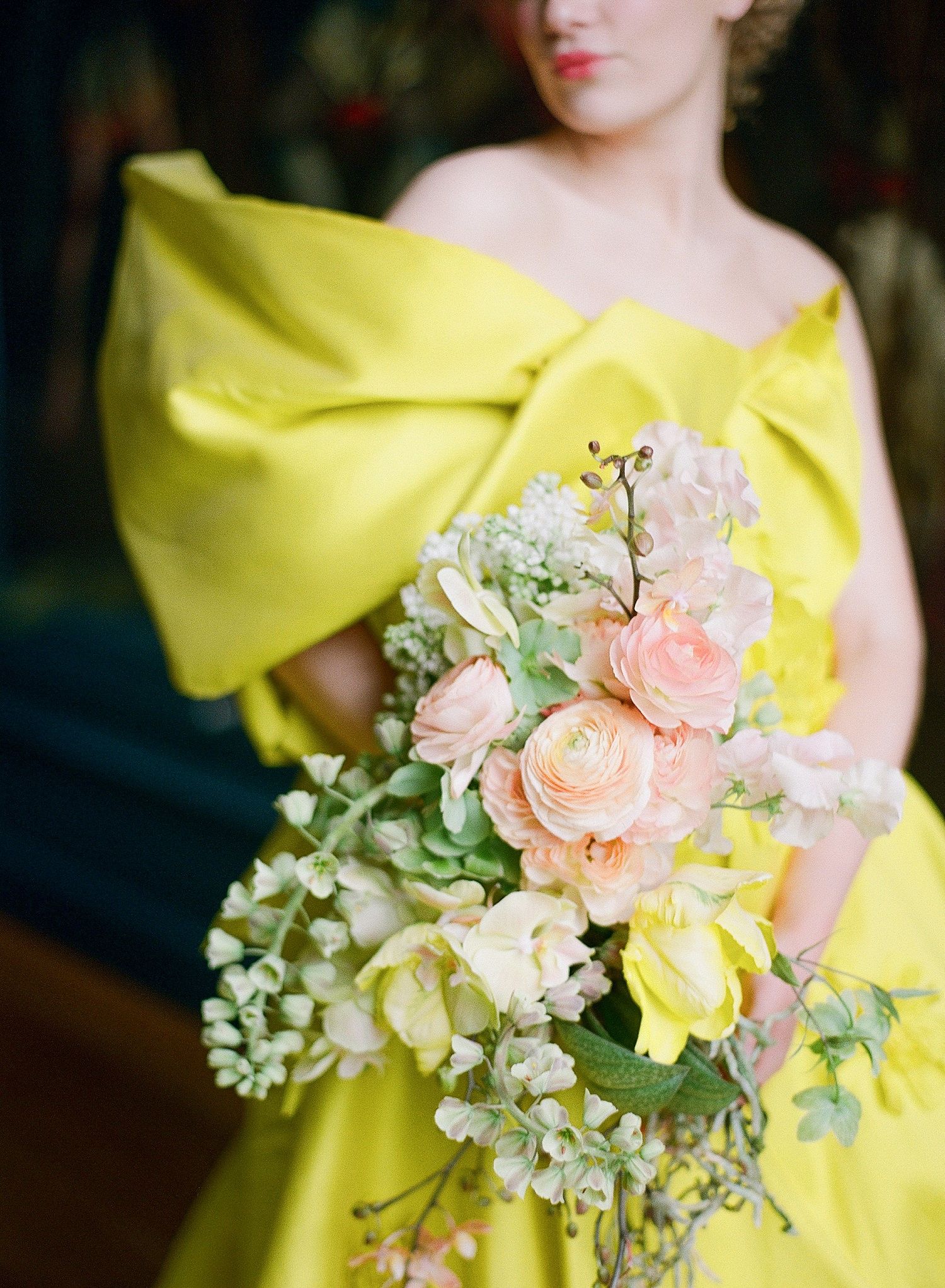 A person wearing a vibrant yellow dress holds a delicate bouquet of peach roses and white flowers.