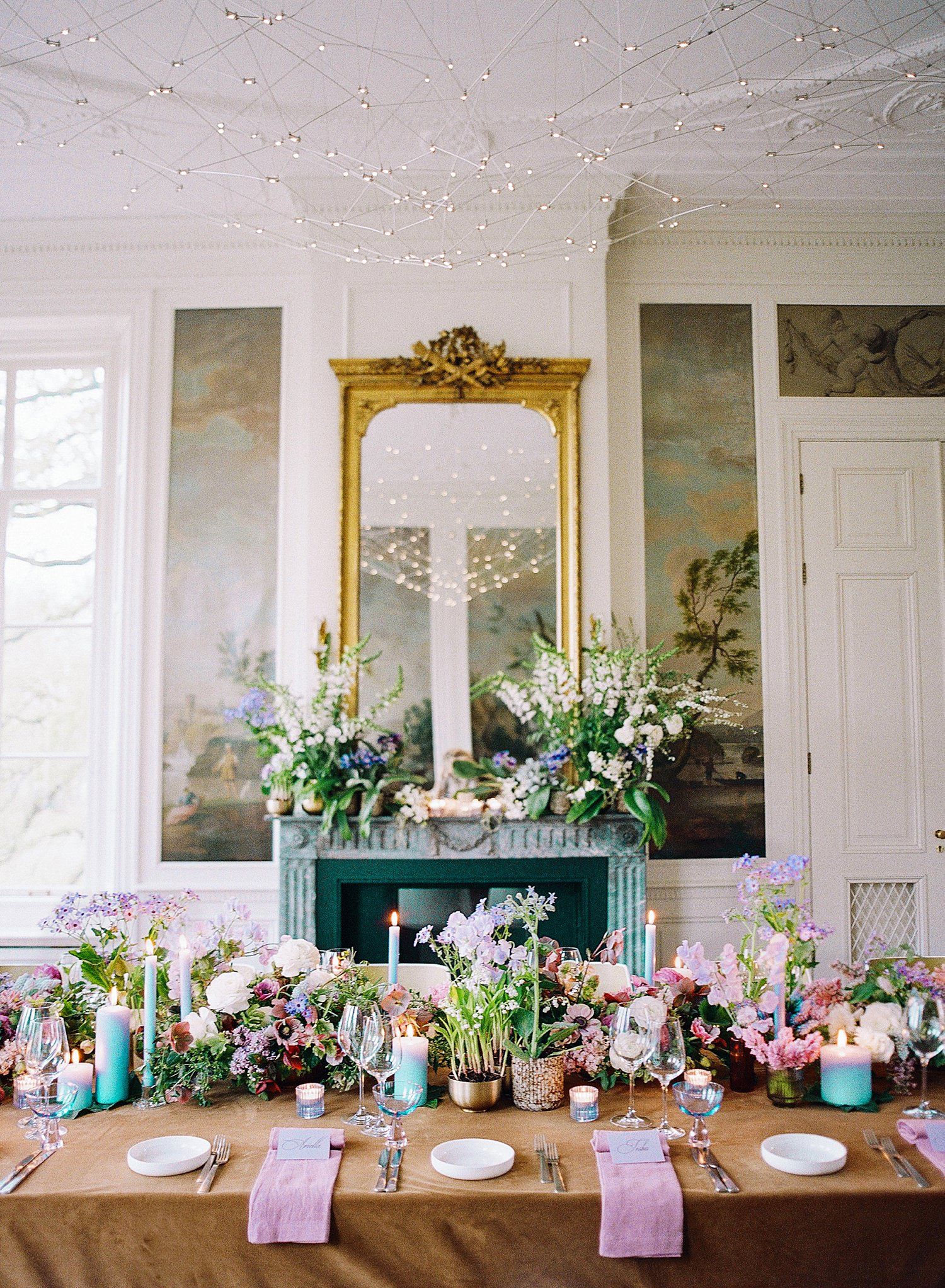 Elegant wedding reception table setting with pastel floral arrangements and gold accents in a historic white room.