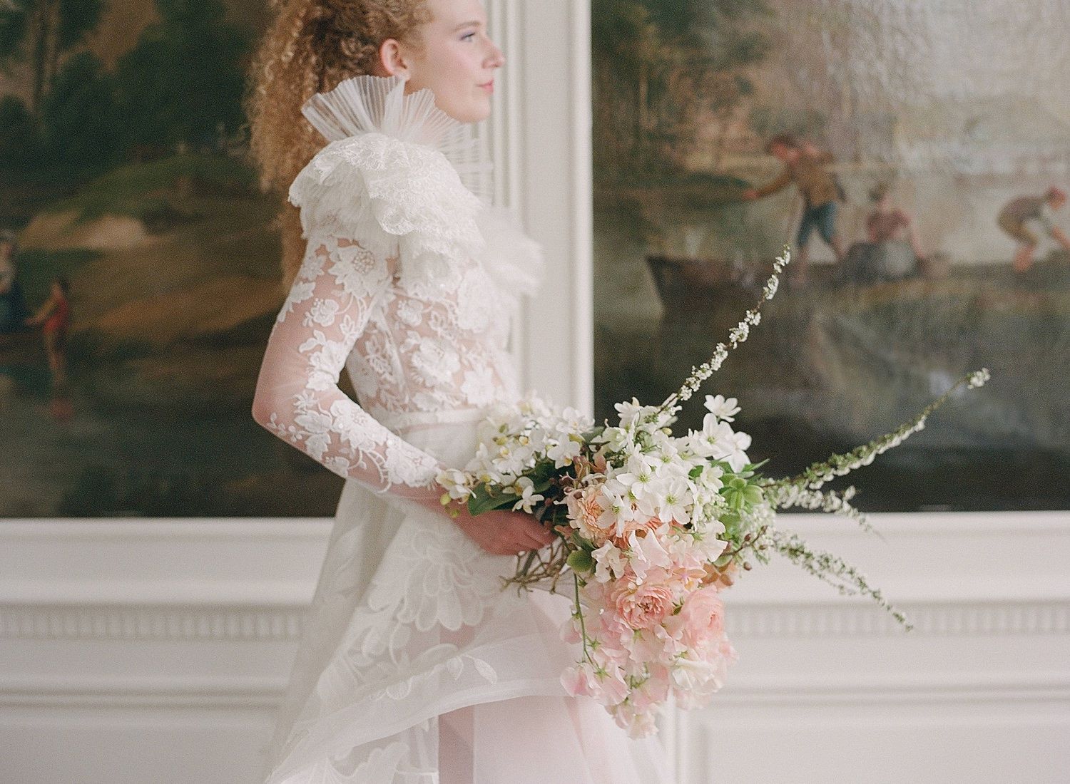 Elegant bridal bouquet with white and pink flowers held against a lace wedding dress in a classic indoor setting.