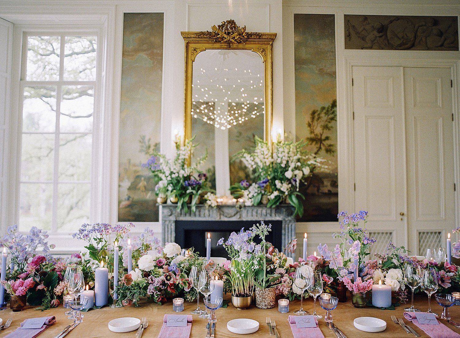 Elegant dining table setup with place settings in a white room with ornate gold frames and floral arrangements.